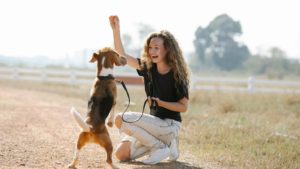 A person kneeling on the ground with a dog Description automatically generated